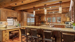 A rustic kitchen with wooden cabinets, a large island with bar stools, and pendant lighting. - Abode at Forest Edge, luxury log home, hot tub (Wilson)