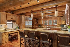 A rustic kitchen with wooden cabinets, a large island with bar stools, and pendant lighting. - Abode at Forest Edge, luxury log home, hot tub (Wilson)