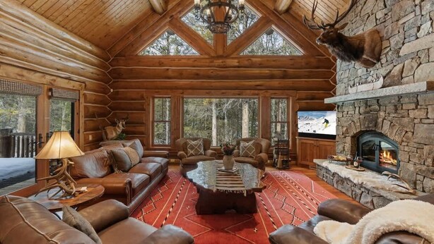 A log cabin interior with a stone fireplace, leather furniture, and a mounted elk head. - Abode at Forest Edge, luxury log home, hot tub (Wilson)