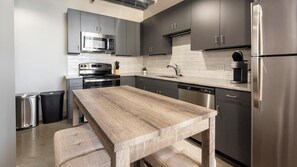 A modern kitchen with stainless steel appliances, dark cabinetry, and a wooden table. - Landing | Stylish 2BD in Uptown (Memphis)