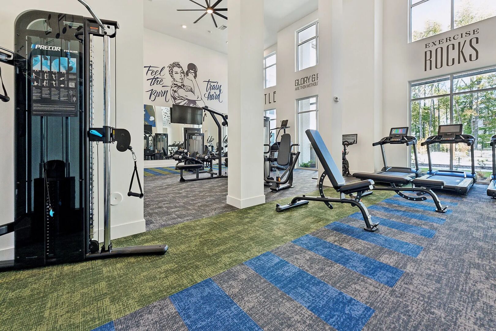 A gym with exercise equipment, motivational wall art, and large windows.