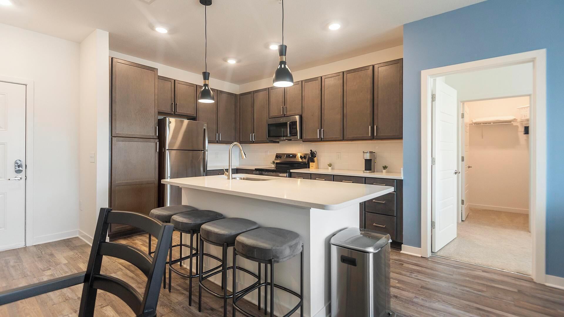 A modern kitchen with a central island, bar stools, stainless steel appliances, and pendant lighting.