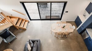 Un interior moderno con una mesa de comedor lista para cuatro personas, un sofá, una escalera y una zona de cocina.
