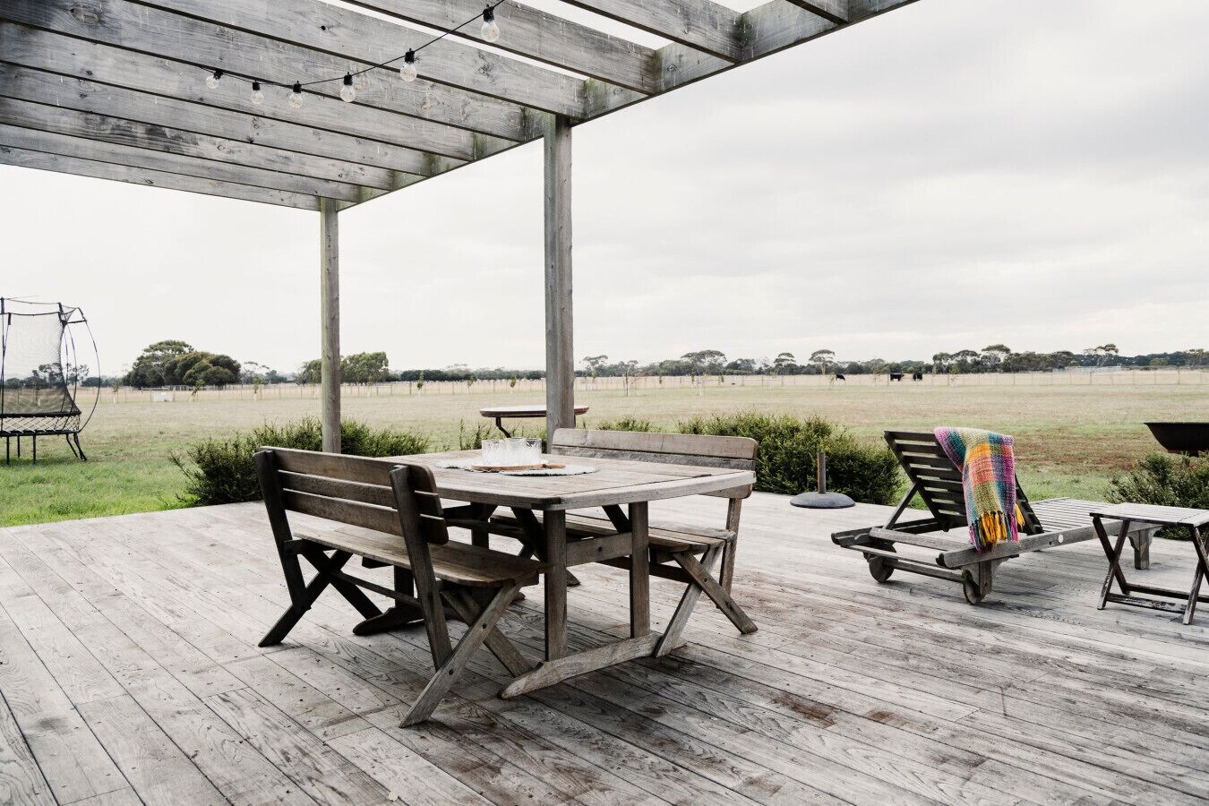 An outdoor wooden deck with a table and benches, overlooking a grassy field.