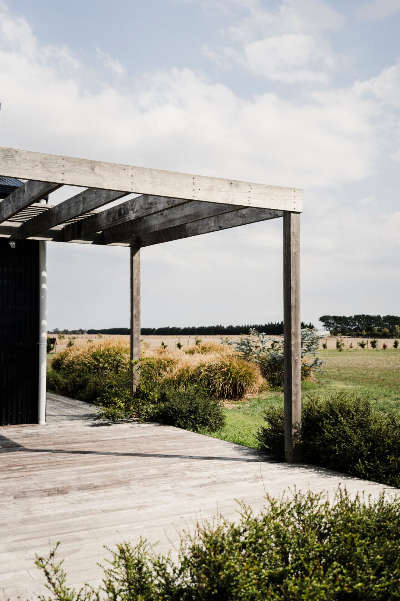 A wooden deck leading to a covered area with a view of a field and trees.