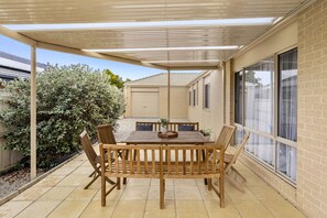 Eine überdachte Terrasse mit Tisch und Stühlen, eine Ziegelwand und ein Fenster.