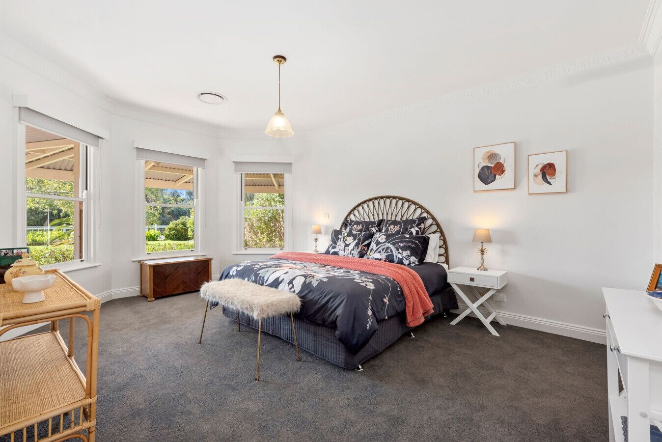 A bedroom with a large bed, two bedside tables, a chair, and a window with a view of greenery.