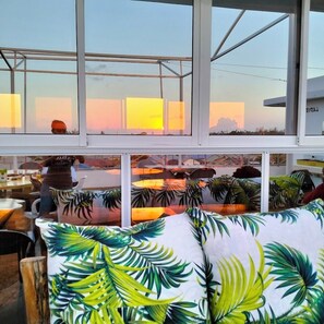 A room with large windows, a view of the sunset, and a tropical leaf-patterned cushion. - RG Hotel Mtongwe (Mombasa)