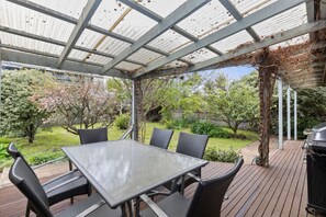 A covered patio with a table and chairs, surrounded by greenery and a barbecue grill. - Matching Green on The Parade - perfect location! (Ocean Grove)