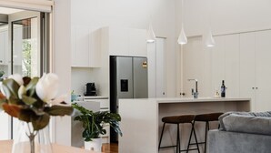 A modern kitchen with a refrigerator, coffee machine, and bar stools. - Seabreeze Pacific Drive - Torquay - Sleeps 11! (Torquay)