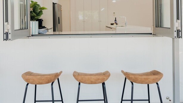 A modern kitchen with three bar stools, a wooden ceiling, and a view of the adjacent room. - Seabreeze Pacific Drive - Torquay - Sleeps 11! (Torquay)