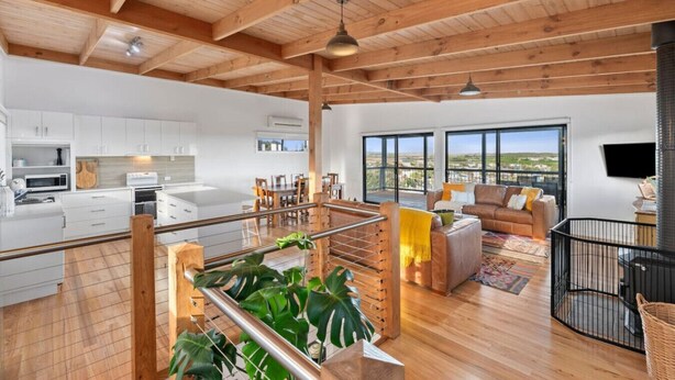 A spacious living area with a high ceiling, a kitchen with white cabinetry, and a balcony with a view. - Ocean Views on Aldebaran - sleeps 11 (Ocean Grove)