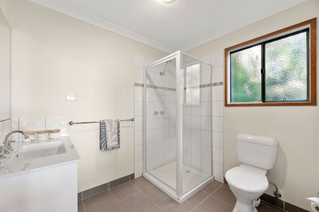 A bathroom with a shower, toilet, sink, and a window with a view.