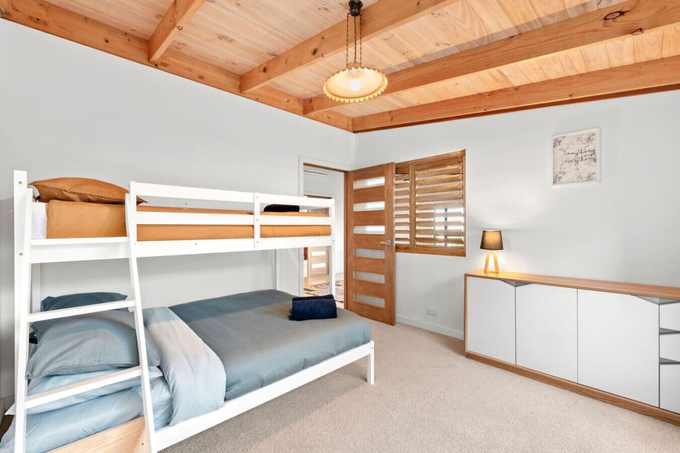 Habitación con literas, techo de madera, un escritorio con lámpara y ventana con persianas.
