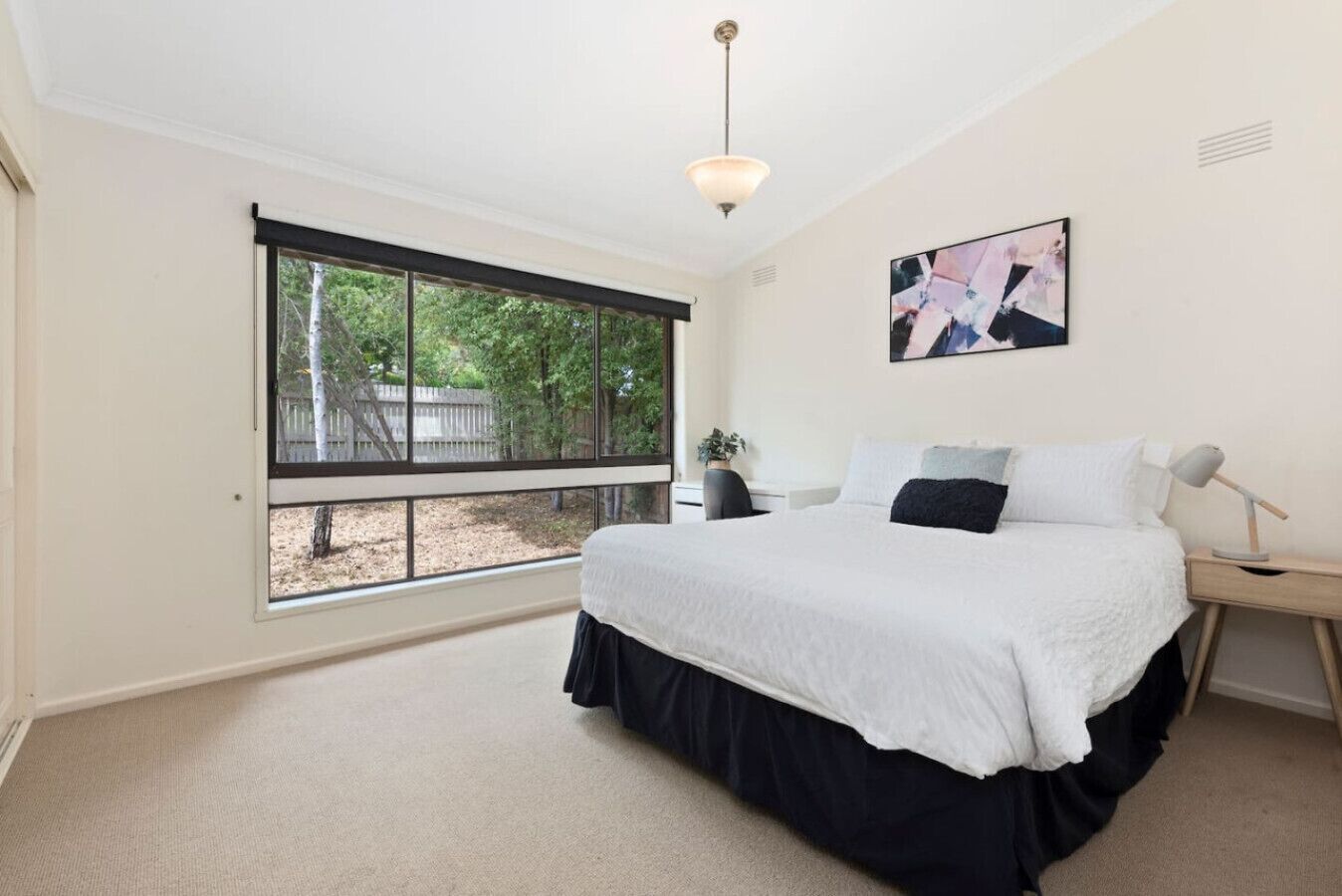 A bedroom with a large window, a bed, a desk, and a chair.