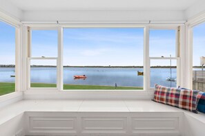 A room with a large bay window overlooking a calm body of water, a small boat, and a grassy area. - Portrush - Ultimate Family Stay - Sleeps 13 (Barwon Heads)