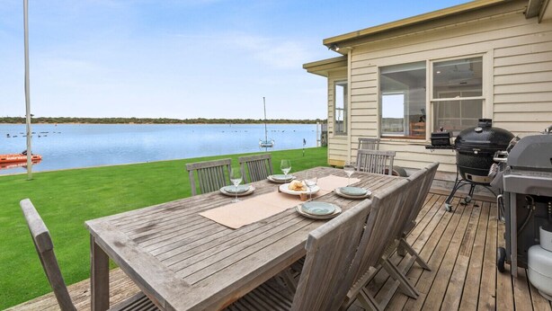 Eine Holzterrasse mit Esstisch, mit Blick auf einen See mit Booten.