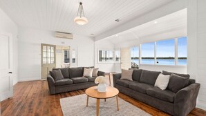 Ein geräumiges Wohnzimmer mit zwei grauen Sofas, einem Holztisch und einem großen Fenster mit Blick auf das Meer.