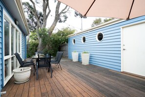 A deck with a table and chairs, a large umbrella, and a garage door. - Riverside Charm - Sleeps 8! (Barwon Heads)