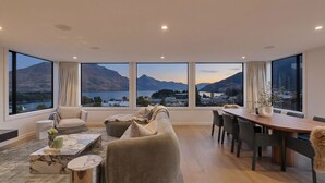 Una sala moderna con un amplio ventanal que ofrece vistas a la montaña y al lago, un sofá, una mesa de comedor y una mesa de centro.