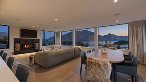 Una sala de estar moderna con chimenea, un sofá grande, una mesa de comedor y vistas a montañas y un lago.