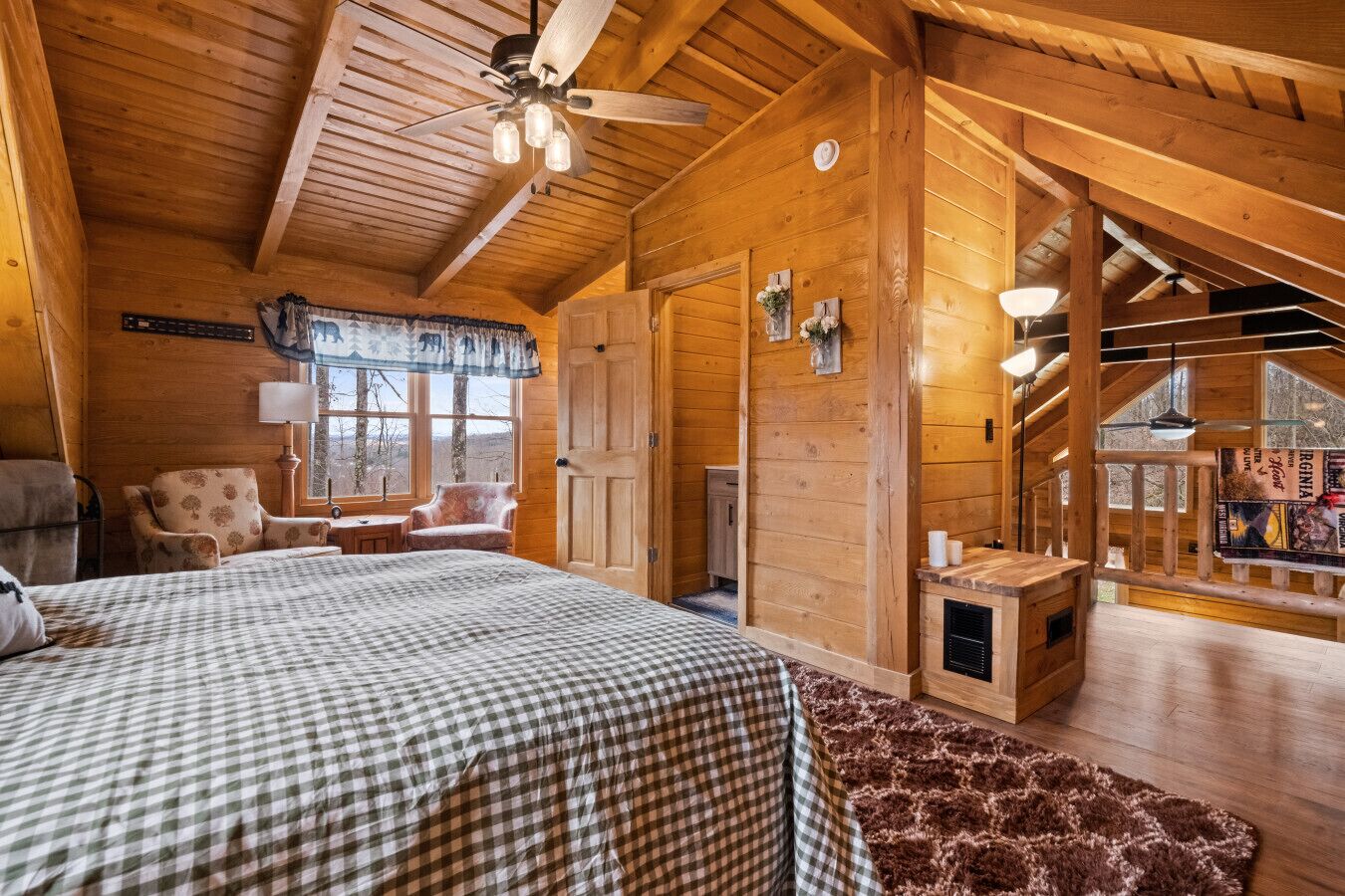 A log cabin bedroom with a bed, two chairs, a window, and a staircase leading to an upper level.