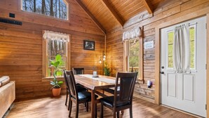 A wooden cabin interior with a dining table, chairs, potted plants, and a door.