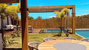 Eine Holzterrasse mit einem runden Tisch, Korbstühlen, einem Pool und einem Holzzaun.