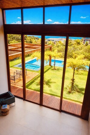 Quarto com grandes janelas com vista para uma piscina e jardim.