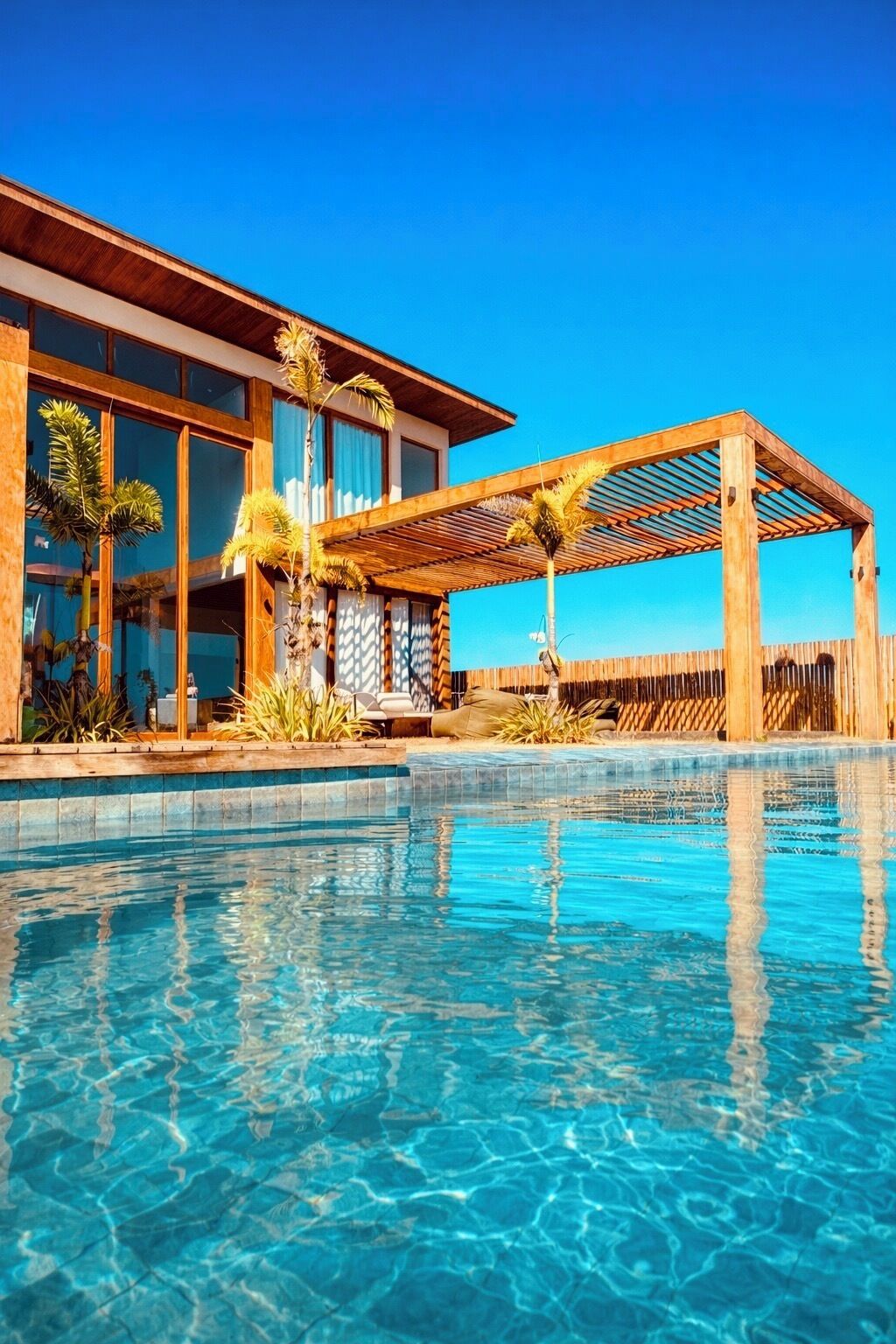 Un hôtel moderne doté d’une piscine, d’une pergola en bois et de plantes tropicales.