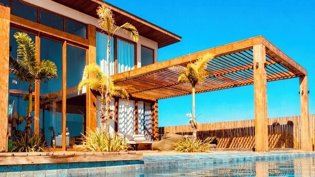 Ein modernes Hotel mit Schwimmbad, einer Holzpergola und tropischen Pflanzen.