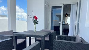 En balkong med möbler i rotting, ett bord och en vas med en blomma.