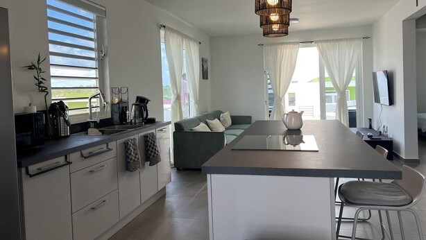 Ett modernt kök med en central köksö, en matplats med soffa och ett stort fönster som släpper in naturligt ljus.