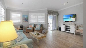 Un salon comprenant un canapé, un fauteuil, une table basse, un téléviseur et un meuble.
