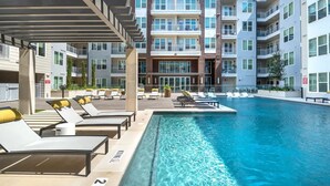 Un hotel moderno con piscina, tumbonas y un edificio de varias plantas con balcones.