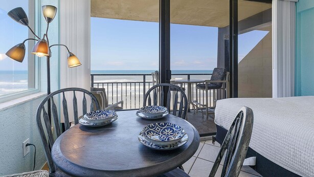 A balcony with a table, chairs, and a bed. - Oceanview Studio w/ Private Balcony, Pools & Beach Access (Daytona Beach Shores)