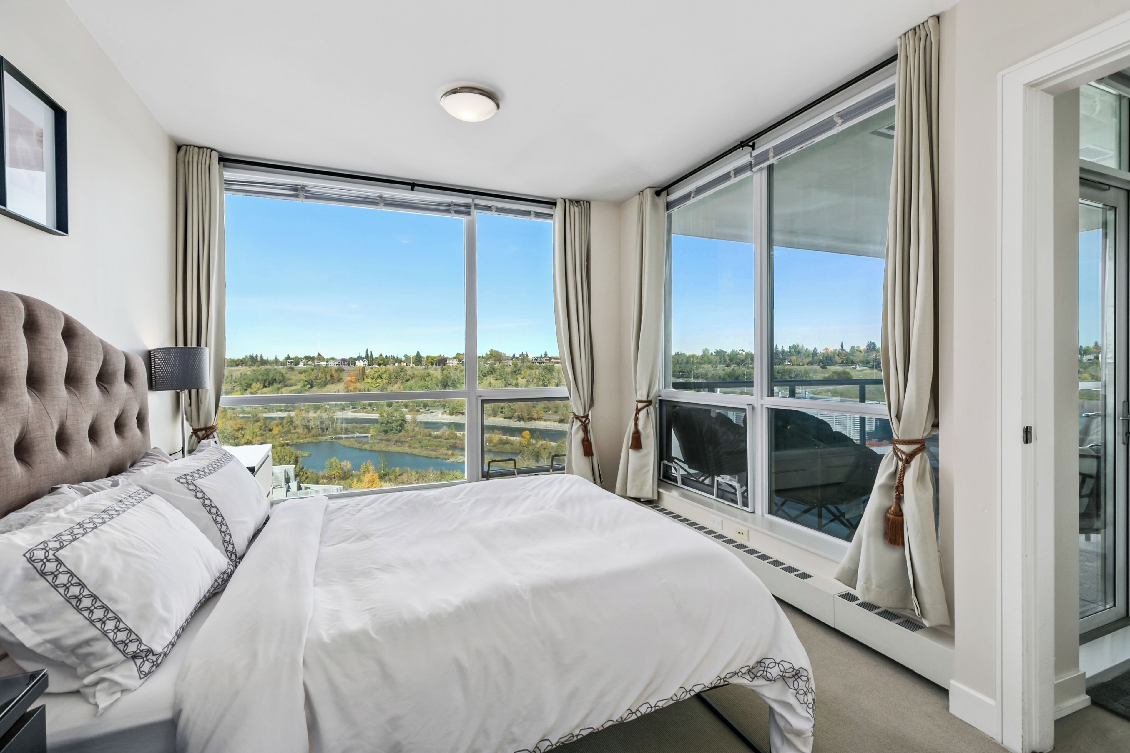 A hotel room with a large bed, a view of a lake, and a balcony with curtains.