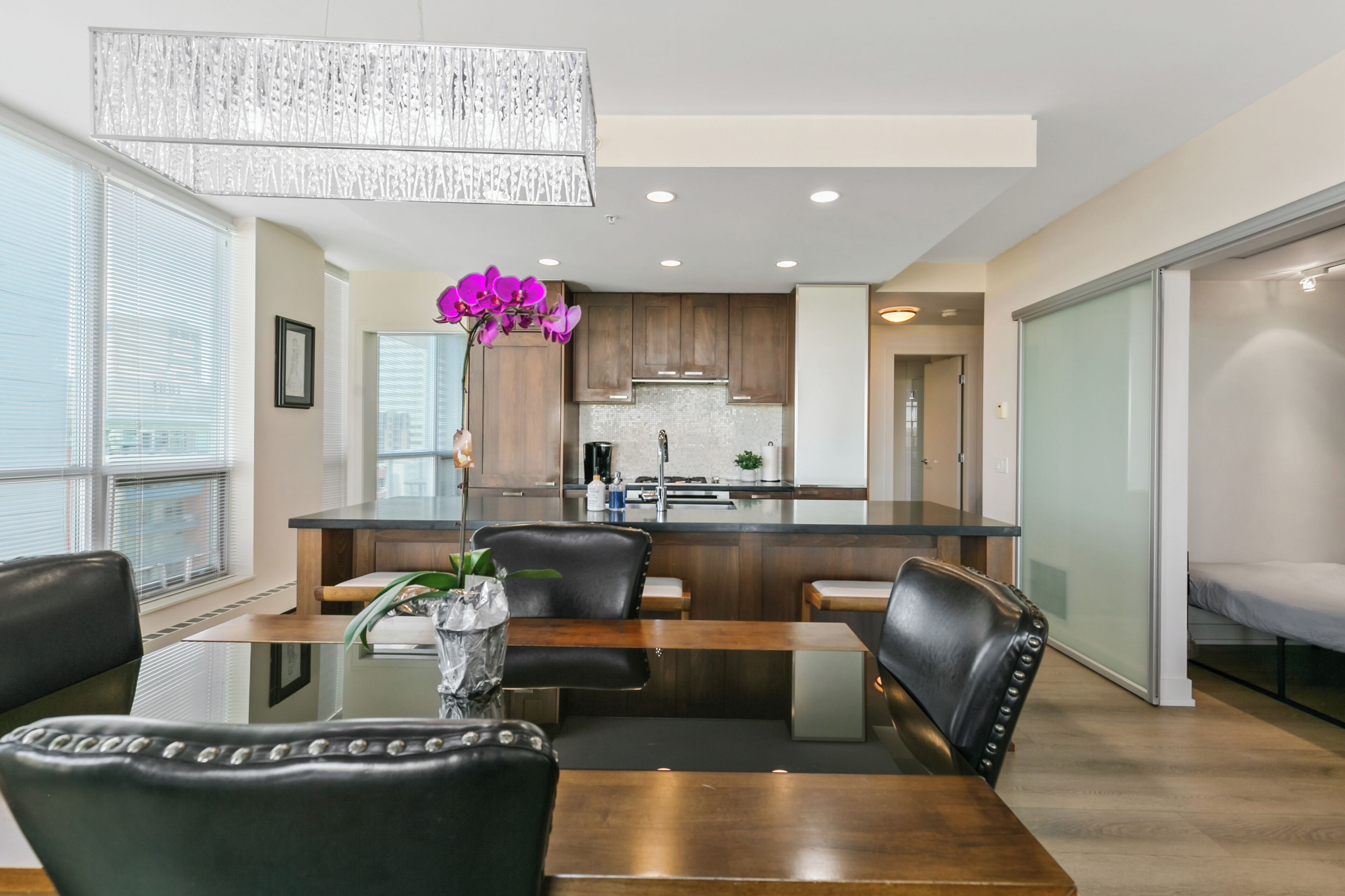 A modern kitchen with wooden cabinets, a central island, and a dining area with a glass table and leather chairs.