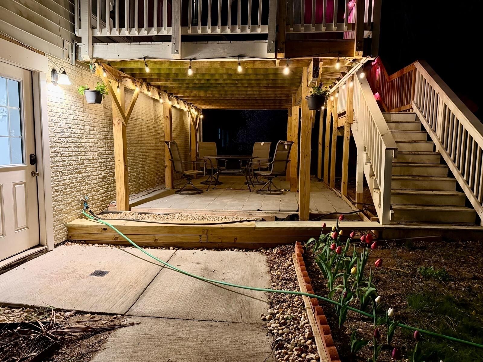A covered patio area with outdoor furniture, a wooden deck, and a staircase leading to an upper level.