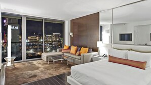 Camera d'albergo moderna con un letto grande, un divano, un tavolino e vista sulla città illuminata di notte.