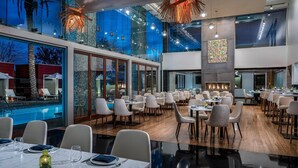 Un'ampia sala da pranzo con diversi tavoli e sedie, ampie finestre e vista sulla piscina.
