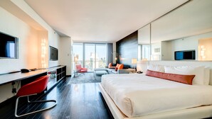 A hotel room with a large bed, a desk with a chair, a TV, and a view of the city. - SVS: Strip View Studio | Open Balcony | Resort Amenities | Palms Place (Las Vegas)