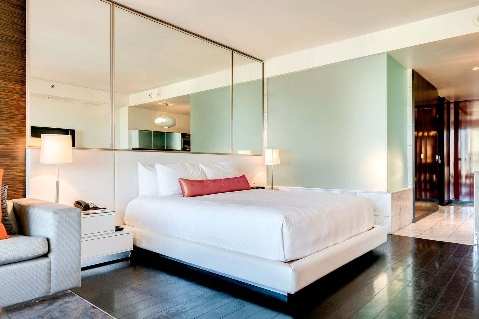 Una camera d'albergo moderna con un letto grande, un comodino con una lampada, una sedia e un ampio specchio.