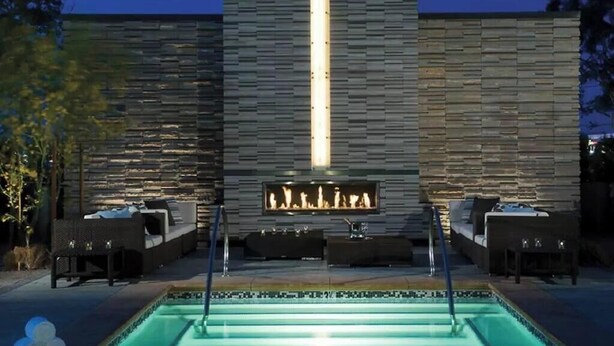 A poolside area with a stone wall, a fire feature, and outdoor seating. - SVS: Strip View Studio | Open Balcony | Pool & Gym | Palms Place (Las Vegas)
