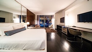 A modern hotel room with a large bed, a desk, a TV, and a view of the city at night. - SVS: Strip View Studio | Open Balcony | Pool & Gym | Palms Place (Las Vegas)