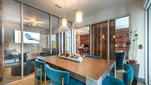 A modern dining area with a long table, blue chairs, and pendant lighting. - Landing | Stunning 2BD, Gym, Game Room (Fort Worth)