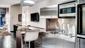 A modern kitchen with stainless steel appliances, a bar area with stools, and a flat-screen TV mounted on the wall. - SVS: Strip View Studio | Open Balcony | Pool & Gym Access | Palms Place (Las Vegas)