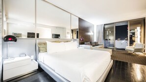 Et moderne hotelværelse med en stor seng, sengeborde, et skrivebord, en stol, et stort spejl og udsigt over byen om natten.