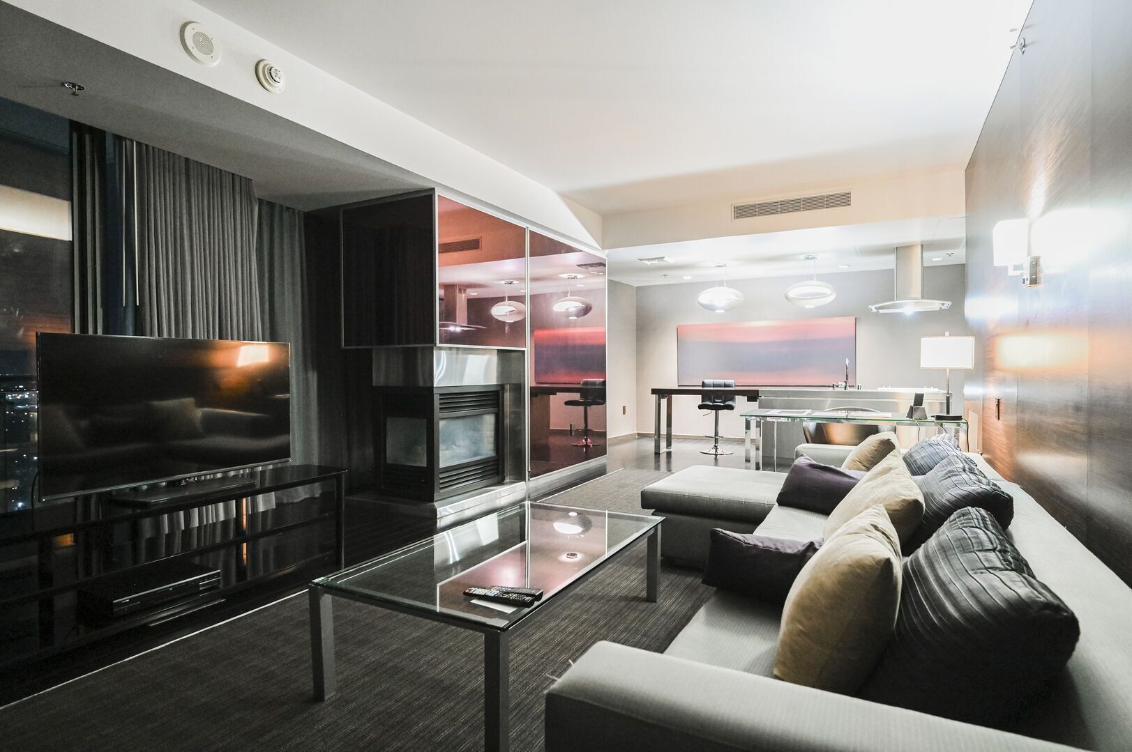 A modern living room with a flat-screen TV, a glass coffee table, a sofa, and a dining area with a table and chairs.