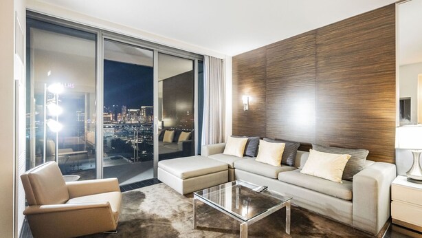 Ein modernes Wohnzimmer mit Sofa, Sesseln und einem Glastisch, große Schiebegläser mit Blick auf die Stadt.